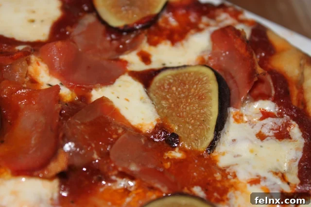 A close-up view of the melted mozzarella, sliced figs, and prosciutto on a grilled crust