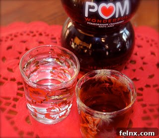 A pomegranate cocktail served on the rocks in a scarlet and grey glass