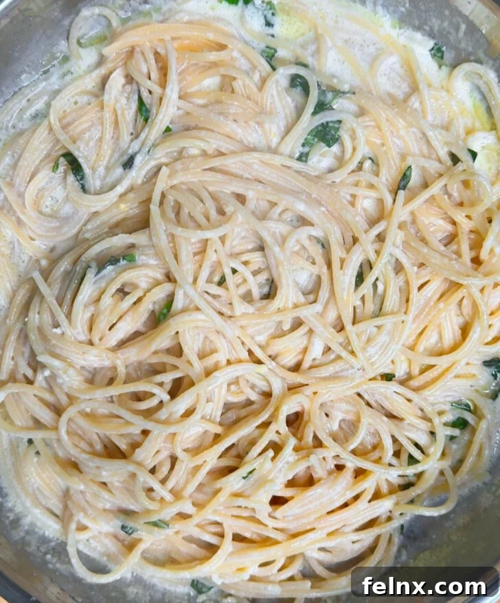 Cooked spaghetti being tossed with the creamy lemon sauce and basil.