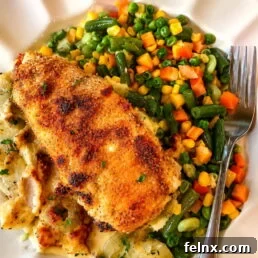 Crispy breaded fish fillet on a creamy bed with a side of mixed vegetables